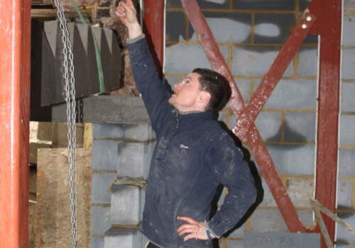 A man points upward while standing in a construction site, surrounded by unfinished walls with various building materials and support structures, indicating focus and communication regarding the task.