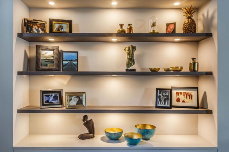 A decorative shelving unit displays various items: framed photos, sculptures, and bowls. The soft lighting highlights these objects against a neutral background, creating a warm, inviting atmosphere.