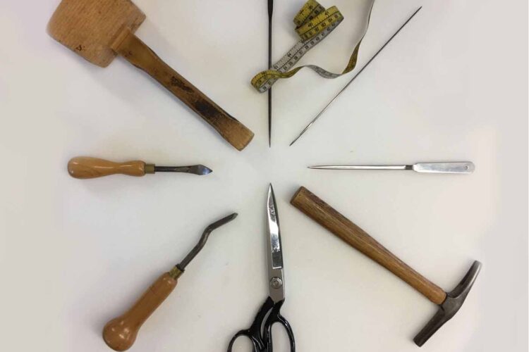 A circular arrangement of various tools includes a wooden mallet, a small chisel, scissors, a measuring tape, and needles, set on a white background, indicating a workspace for crafting or repair.