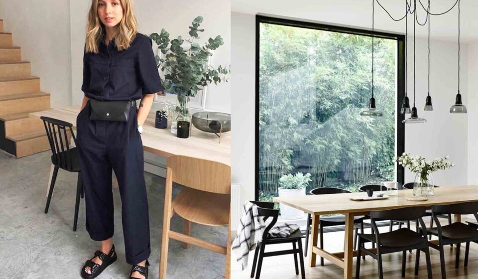 A woman in a dark outfit stands confidently beside a wooden dining table. Natural light streams in from a large window, illuminating a modern, minimalistic dining area with plants and elegant decor.