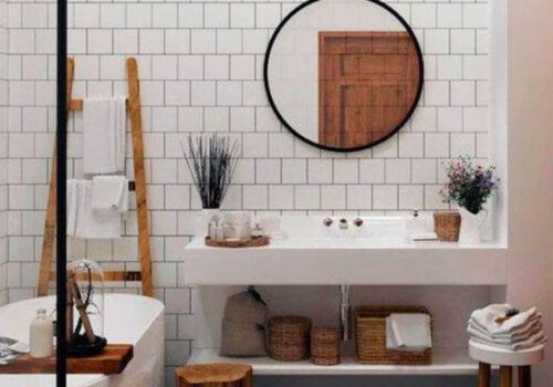 A modern bathroom features a white tiled wall, a round mirror above a sleek sink, and a freestanding tub. Wooden accents include a ladder for towels and a stool, creating a cozy atmosphere.