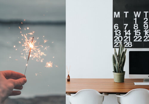 A hand holds a lit sparkler, producing bright sparks against a blurred, gray background. Adjacent, a minimalist workspace features a calendar, a potted plant, and a computer on a wooden desk.