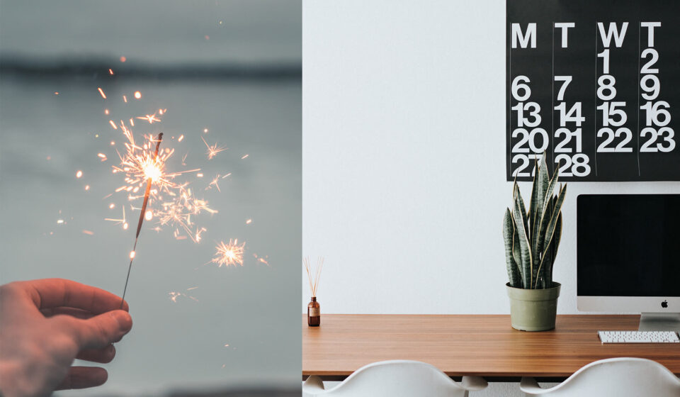 A hand holds a lit sparkler, producing bright sparks against a blurred, gray background. Adjacent, a minimalist workspace features a calendar, a potted plant, and a computer on a wooden desk.