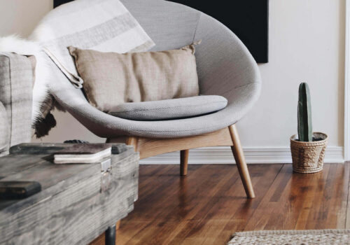 A wooden chair with gray cushions and a decorative pillow sits in a cozy living room