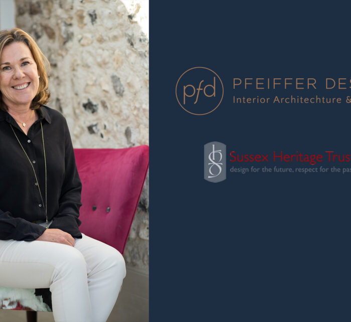 A woman smiles while sitting on a colorful chair in a well-lit room with a textured stone wall behind her, promoting interior design services.