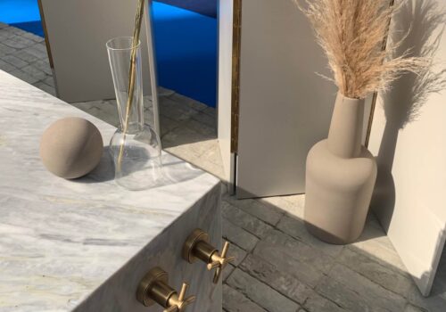 A marble countertop features a round stone and a glass vessel holding a dried plant. Nearby, a cylindrical vase displays pampas grass, all set in a softly lit, modern space.