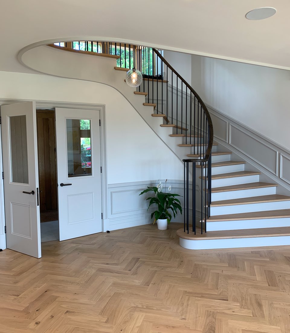 A curved staircase with wooden steps ascends to a landing in a well-lit foyer. Two white doors open to an adjacent room, while a potted plant adds greenery to the space.