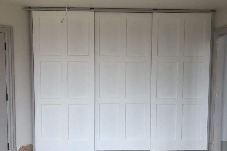 A set of three white, paneled sliding doors is positioned against a neutral wall. The surrounding area shows unfinished flooring and a partially framed doorway on the right.