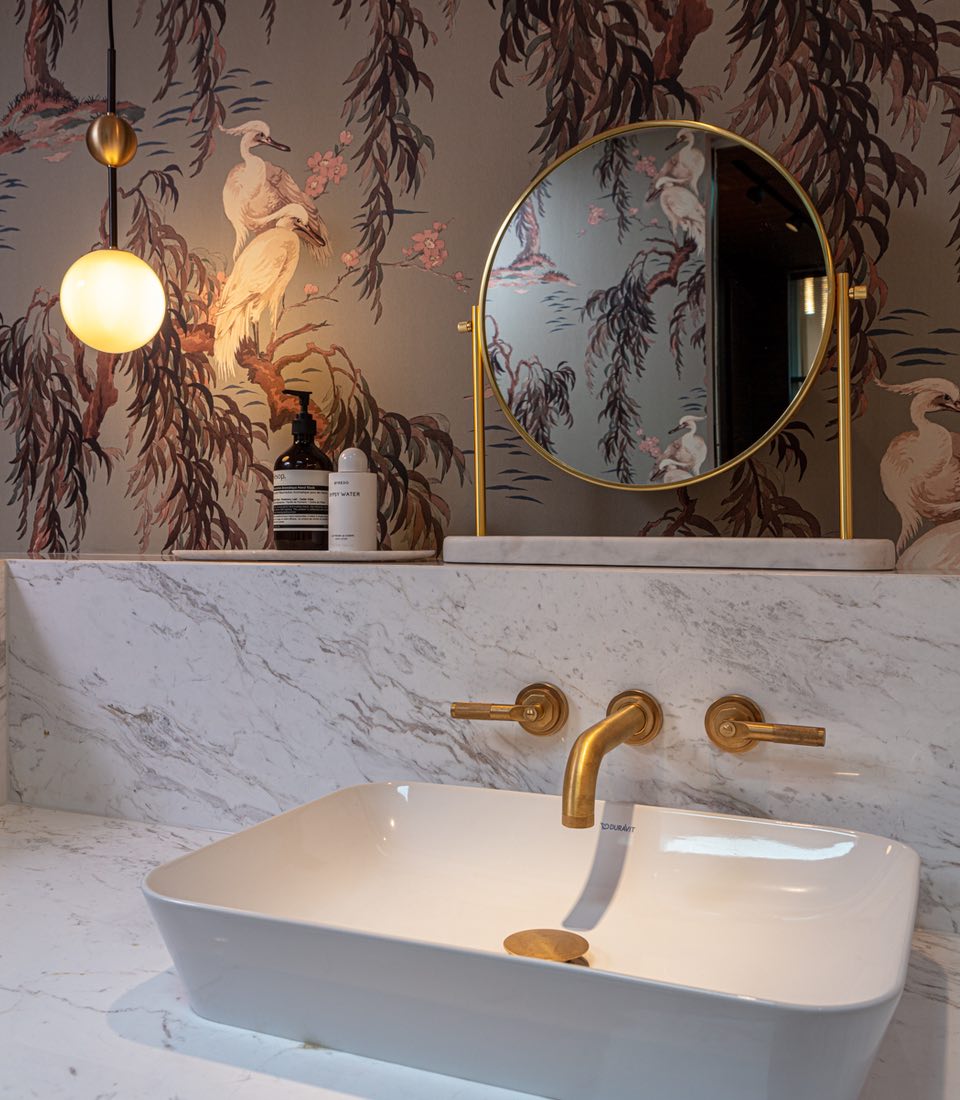 Marble sink surround with brass fixtures and round freestanding mirror