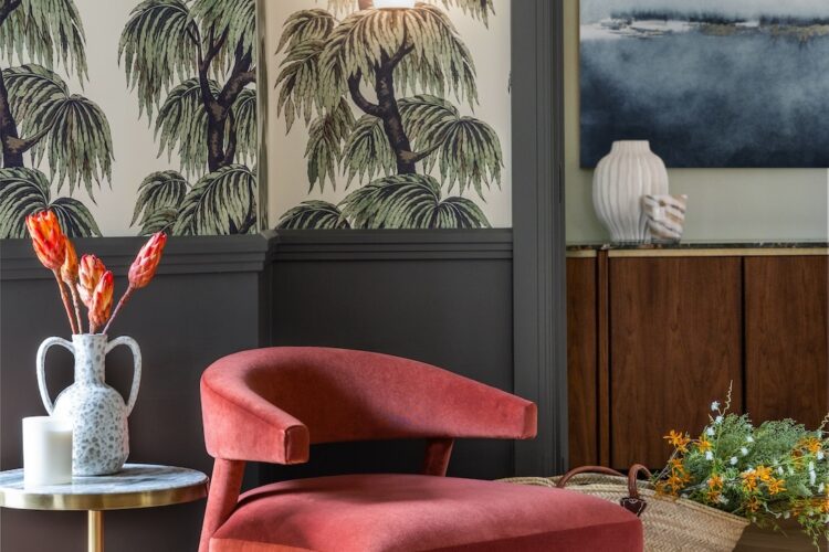 Art Deco Inspired Entrance Hall designed by Pfeiffer Design. Art deco inspired wallpaper, half height panelling and glazed French double doors in deep green. Bronze obscured glass wall lights. A soft red occasion chair with side table with dried flowers in a double handled vase.