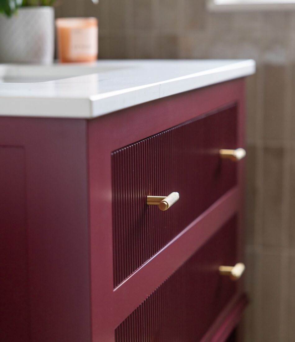 Art Deco Inspired Guest Bathroom/ Downstairs WC designed by Pfeiffer Design. Textured wallpaper in pale pink with half height tiling below, deep burgundy vanity unit with gold accent handles, warm wall lighting in a guest downstairs bathroom WC