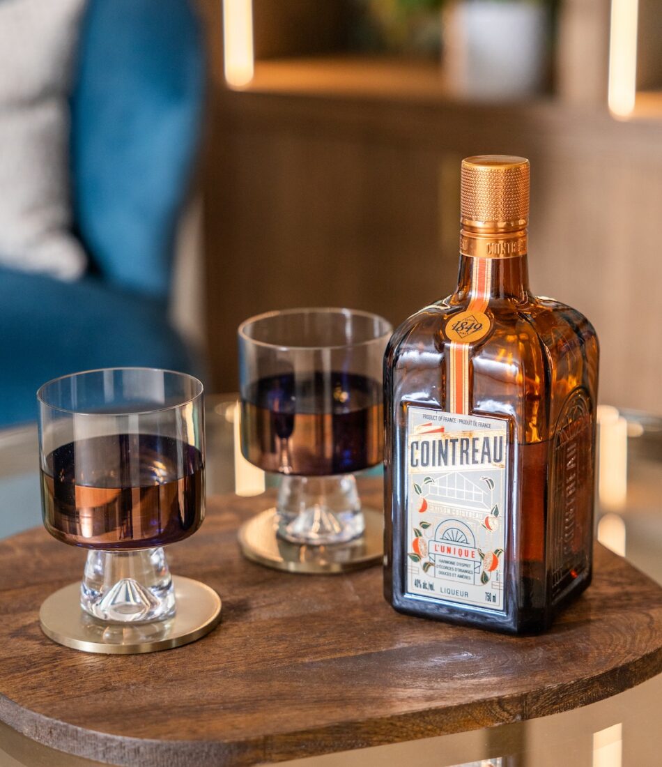 Art Deco Inspired Bespoke Bar and Library made by our bespoke joiners, designed by Pfeiffer Design. Foreground is bottle of drink and beautiful bronze glasses. Background is an art deco inspired joinery piece with LED lighting for a warm but subtle glow