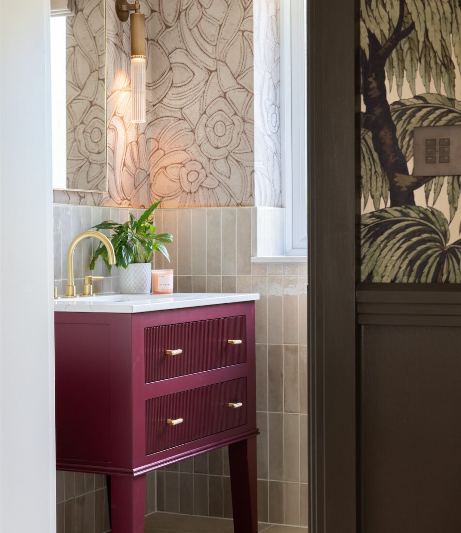 Art Deco Inspired Guest Bathroom/ Downstairs WC designed by Pfeiffer Design. Textured wallpaper in pale pink with half height tiling below, deep burgundy vanity unit with gold accent handles, warm wall lighting in a guest downstairs bathroom WC