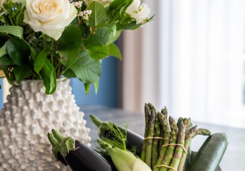 Art Deco Inspired Bespoke Kitchen made by our bespoke joiners, designed by Pfeiffer Design. Bespoke Joinery Kitchen with stone top island. Bunch of flowers in a spiky white ceramic vase and a selection of vegetables in a wavy ceramic white bowl