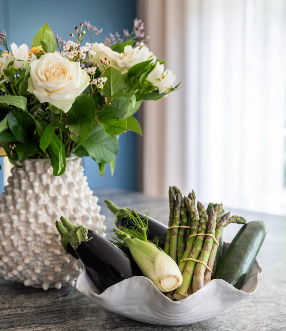 Art Deco Inspired Bespoke Kitchen made by our bespoke joiners, designed by Pfeiffer Design. Bespoke Joinery Kitchen with stone top island. Bunch of flowers in a spiky white ceramic vase and a selection of vegetables in a wavy ceramic white bowl