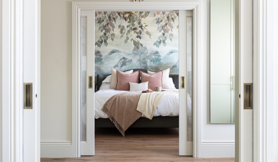 View of principal bedroom through sliding pocket doors, pink and blue tones with scenic wallpaper