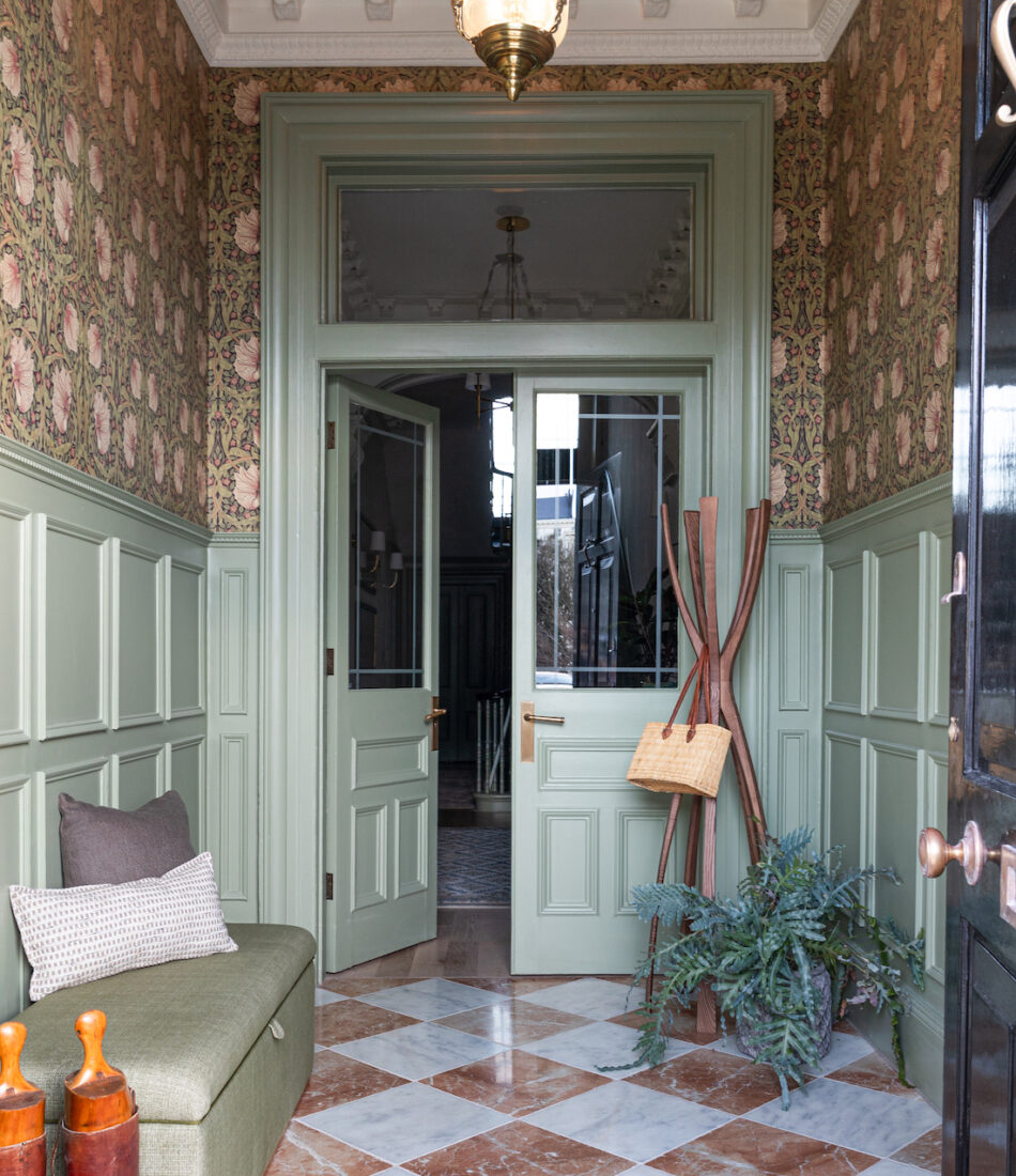 Entrance Hall with traditional half height panelling and detailed wallpaper- green paint and wallpaper tones of red, orange, green, Green upholstered ottoman bench with an umbrella stand