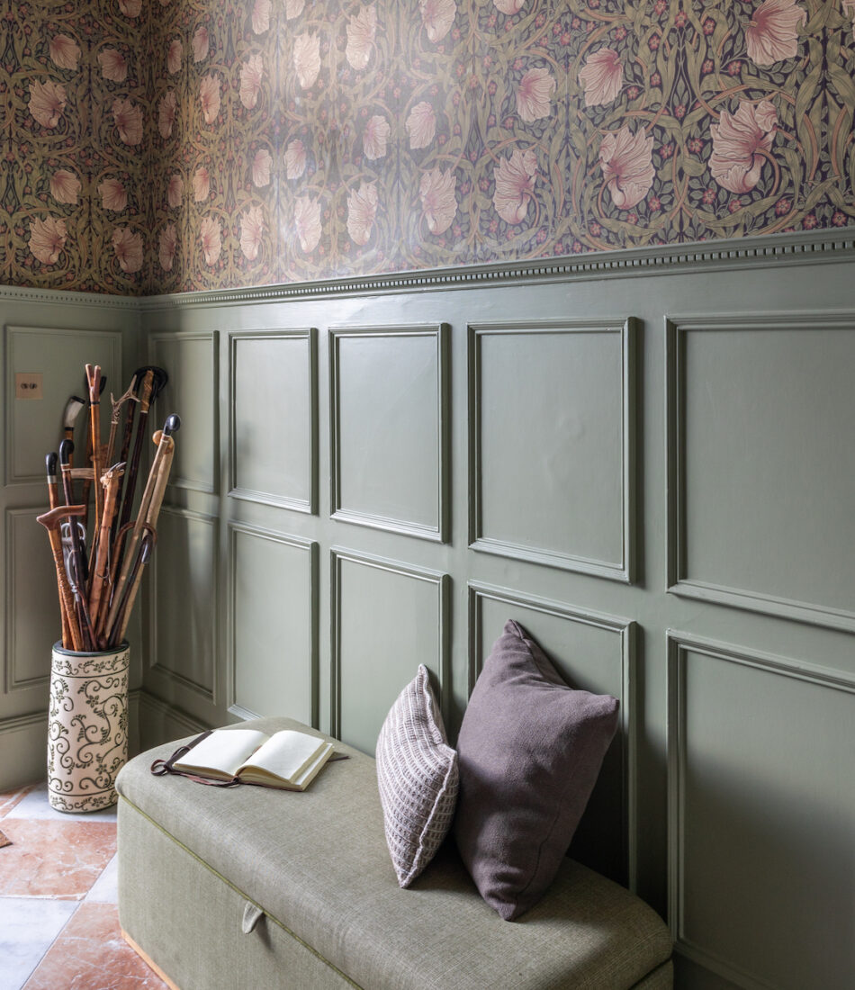 Entrance Hall with traditional half height panelling and detailed wallpaper- green paint and wallpaper tones of red, orange, green, Green upholstered ottoman bench with an umbrella stand