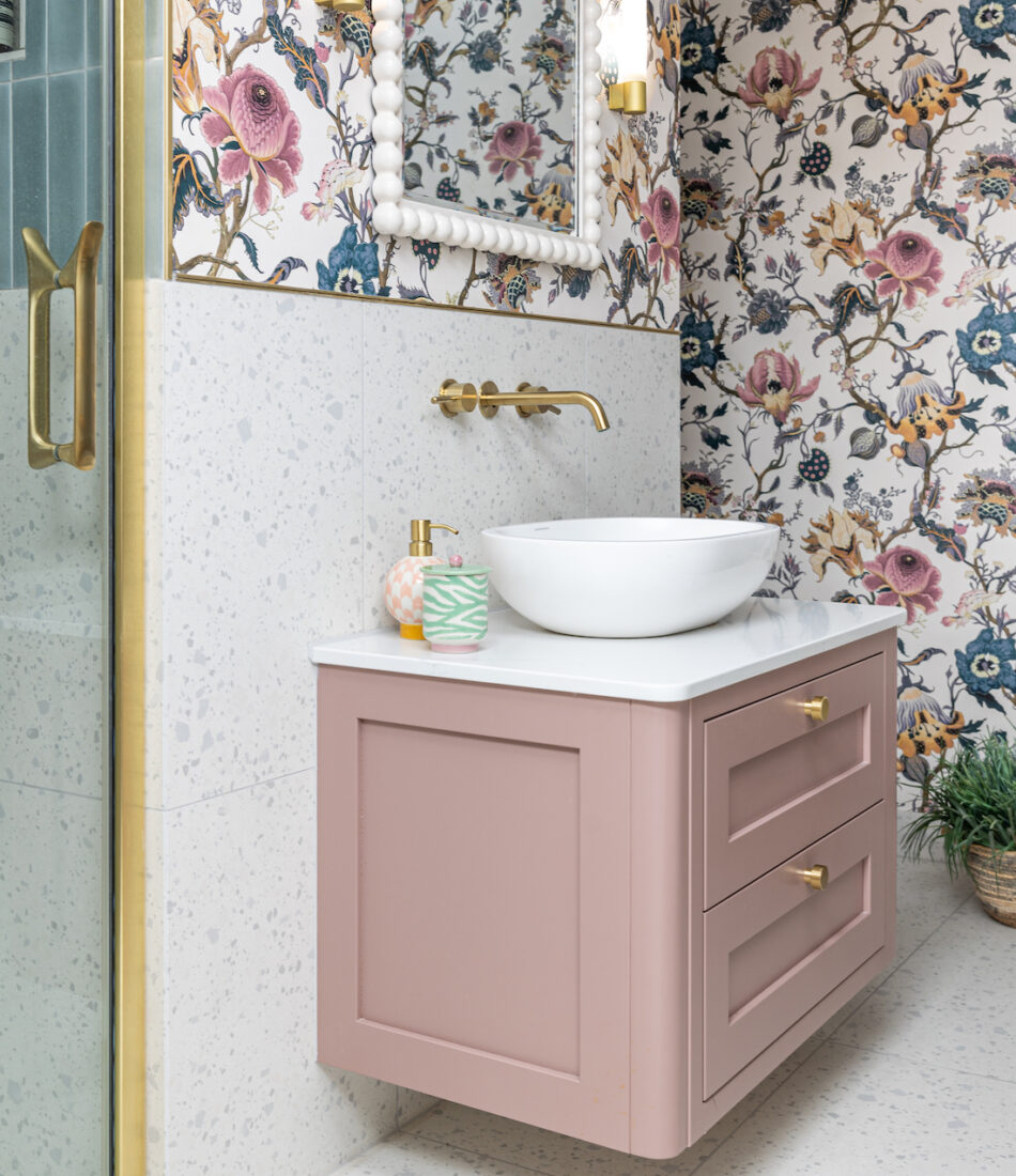 Girls en-suite with floral wallpaper matching the headboard, pink vanity unit and gold hardware
