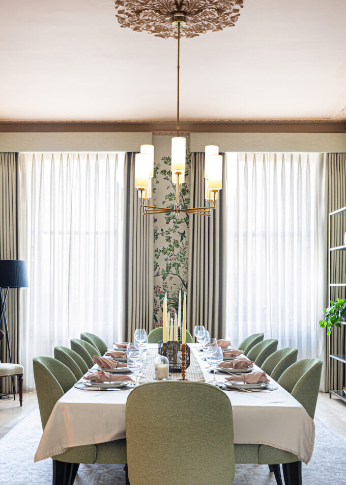 Grand Regenecy townhouse dining room with pink ceiling and cornice, bold patterned tree wallpaper and a set dining table with green chairs, candles, crockery