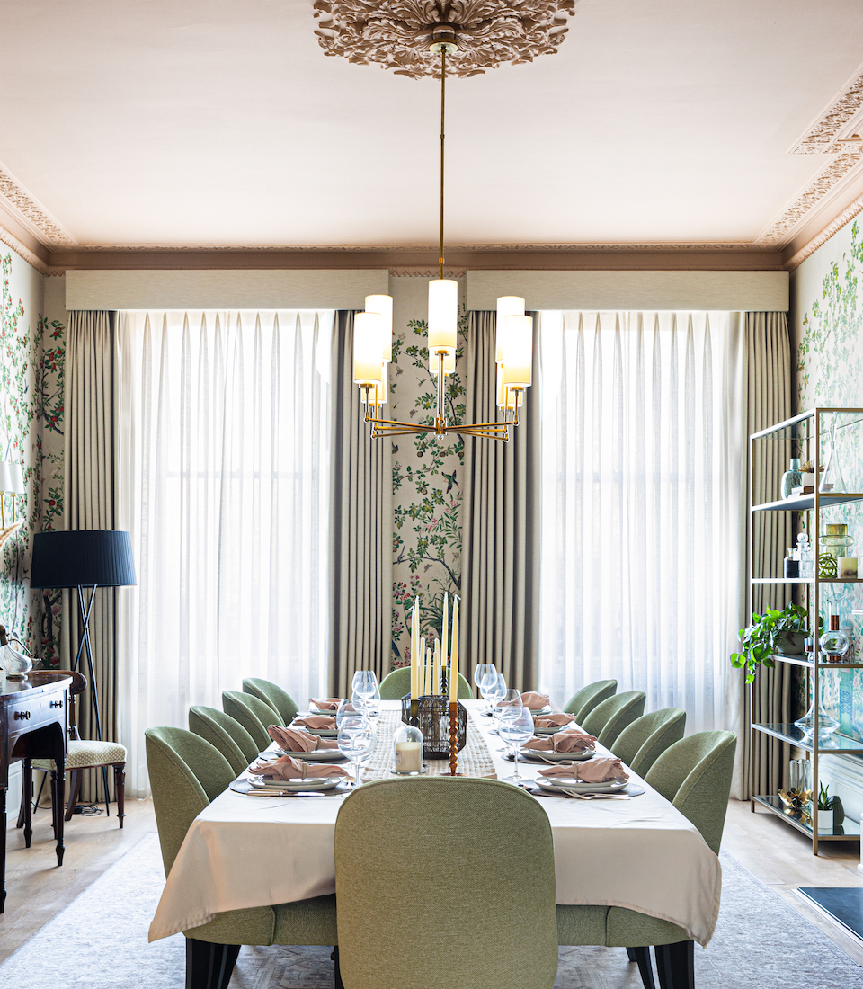 Grand Regenecy townhouse dining room with pink ceiling and cornice, bold patterned tree wallpaper and a set dining table with green chairs, candles, crockery