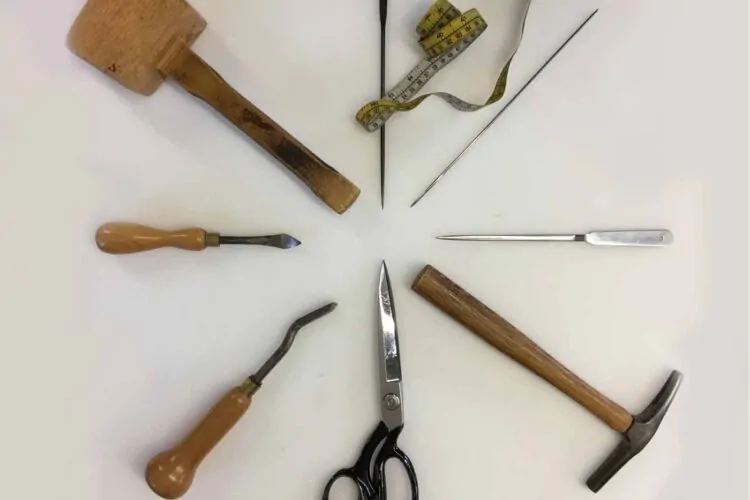 A circular arrangement of various tools includes a wooden mallet, a small chisel, scissors, a measuring tape, and needles, set on a white background, indicating a workspace for crafting or repair.