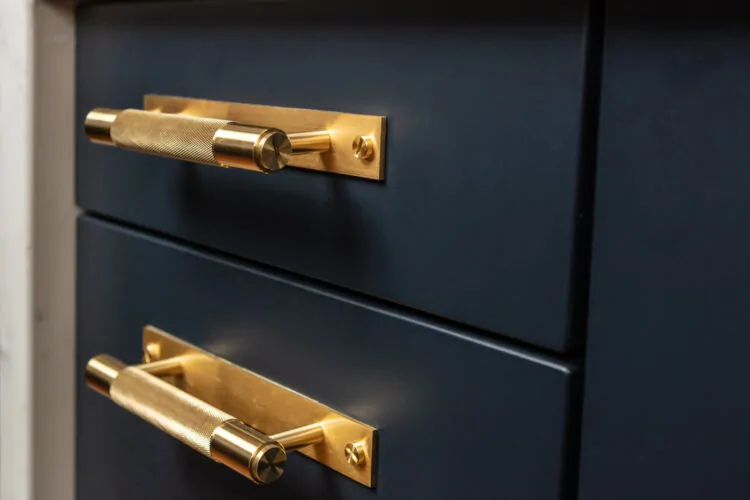 Two gold drawer handles are attached to a dark blue cabinet, positioned horizontally on the front of drawers, suggesting easy access to the storage space within.