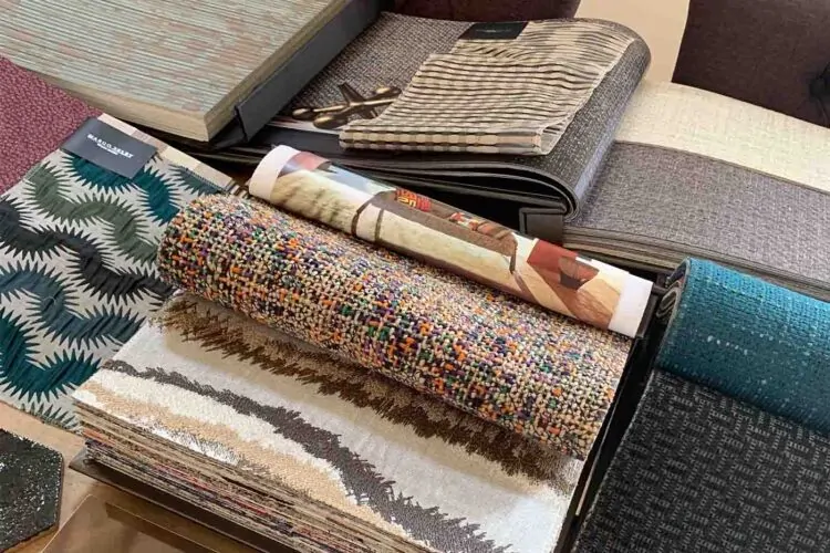 Fabric samples are spread out on a table, showcasing various textures and colors, as a pair of scissors lies nearby, suggesting a design or selection process in a home or studio environment.