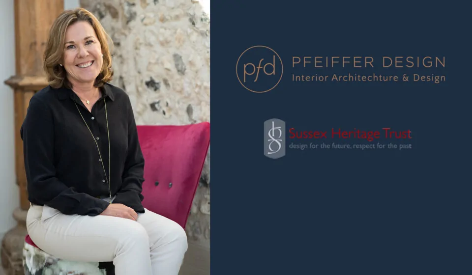 A woman smiles while sitting on a colorful chair in a well-lit room with a textured stone wall behind her, promoting interior design services.