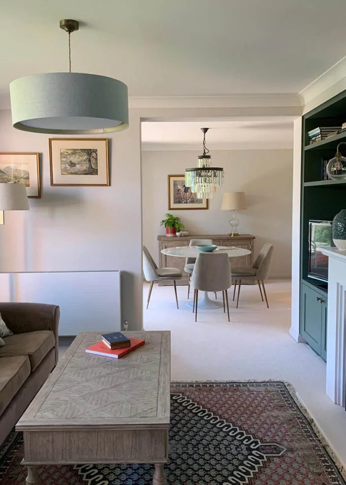 Bright and elegantly decorated living and dining area with modern furnishings, green built-in shelves, pendant lighting, and neutral-toned walls.