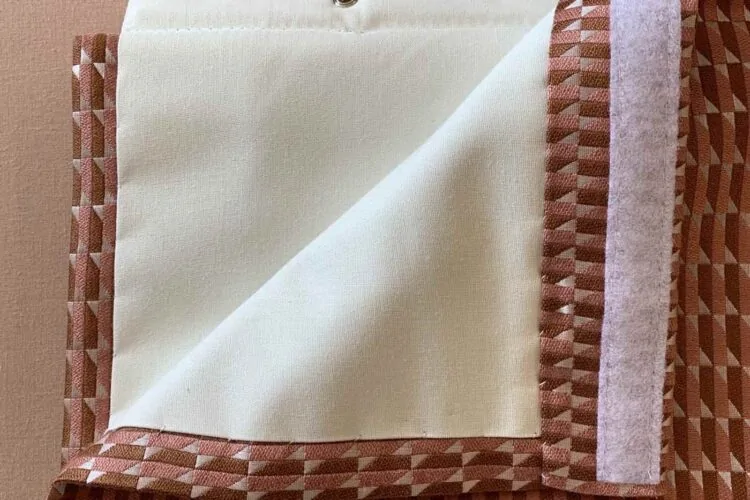 A folded piece of fabric features a patterned brown and pink side and a smooth cream side, showcasing contrasting textures and colors against a light beige background.