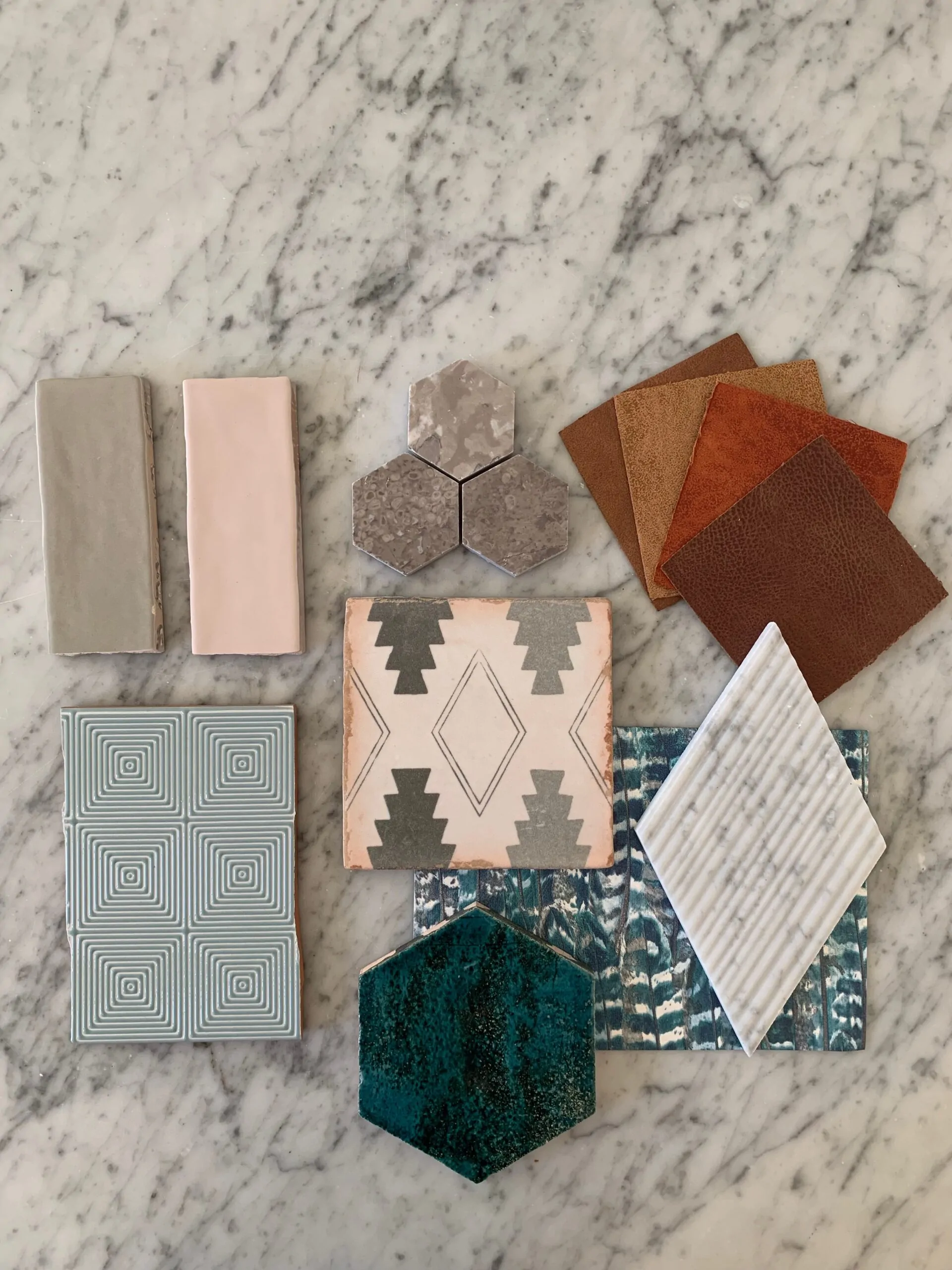 A variety of tiles and textured materials are arranged on a marble surface, including hexagonal, square, and rectangular shapes in different colors and patterns, showcasing design options for flooring or walls.