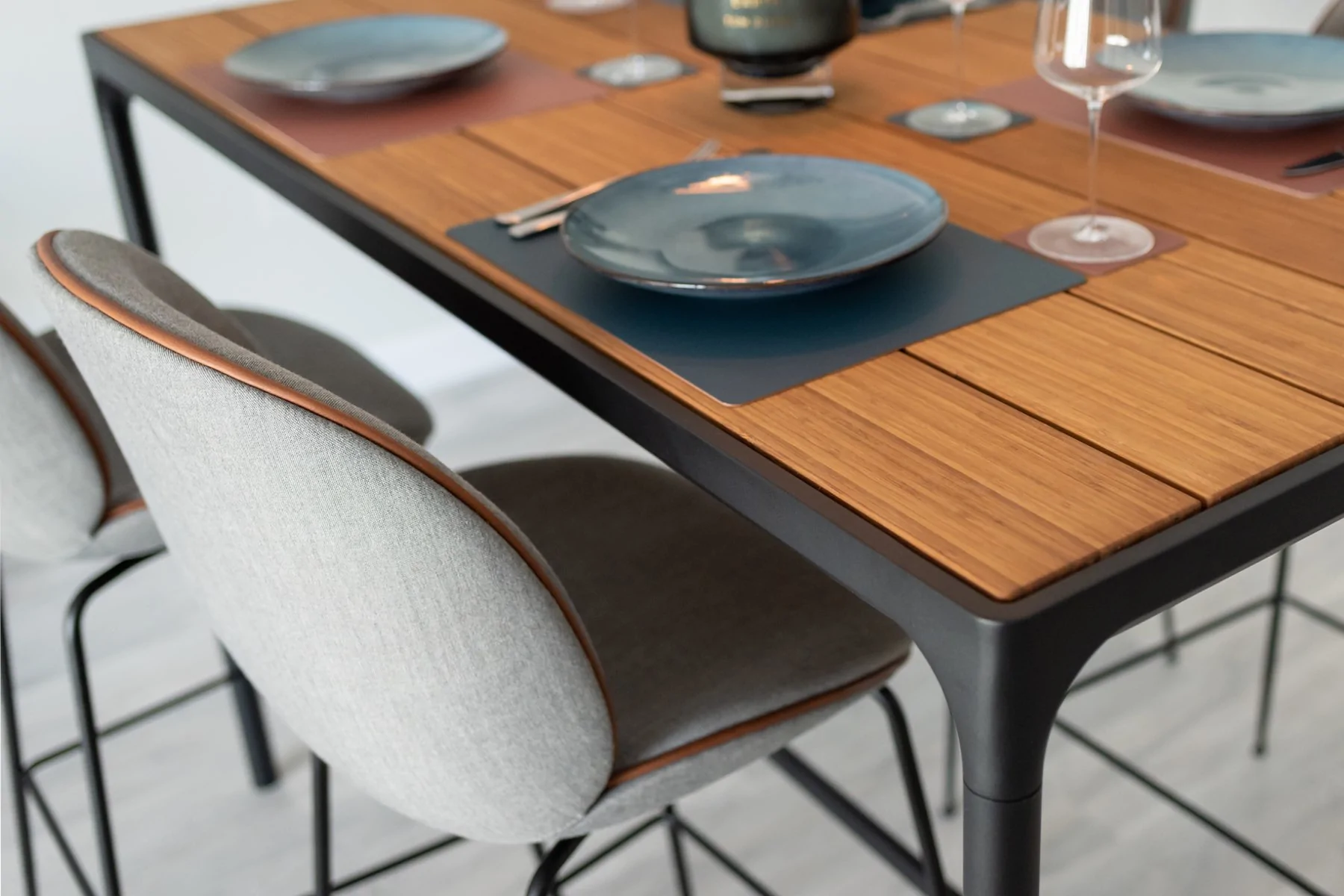 A dining table with a wooden surface is set for a meal, featuring plate settings, glasses, and decorative items. Two upholstered chairs with metal legs are positioned beside it.