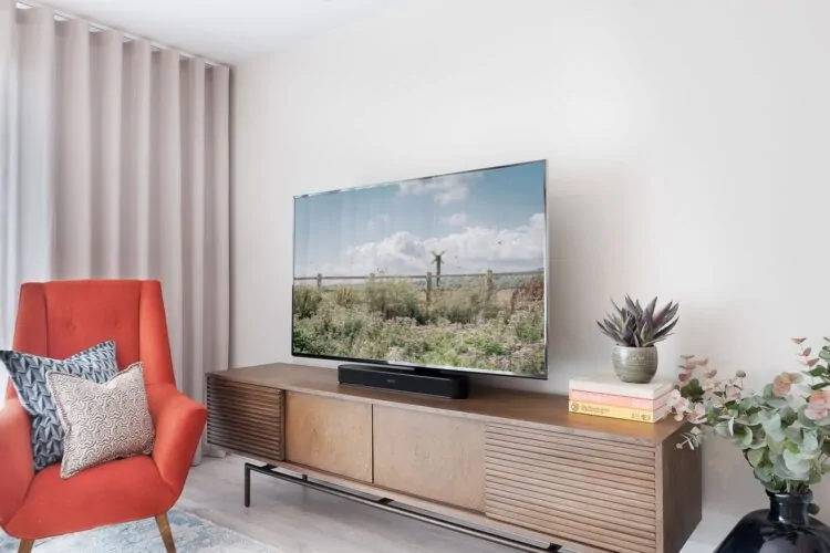 A modern television displays a scenic outdoor landscape, positioned above a wooden media console. Nearby, a bright red armchair and decorative plants enhance the cozy living room ambiance.