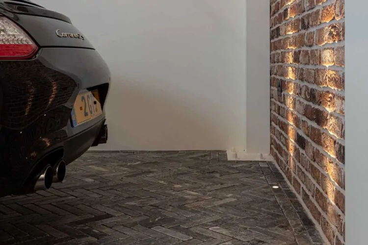 View of high end garage with exposed brick wall and herringbone stone flooring