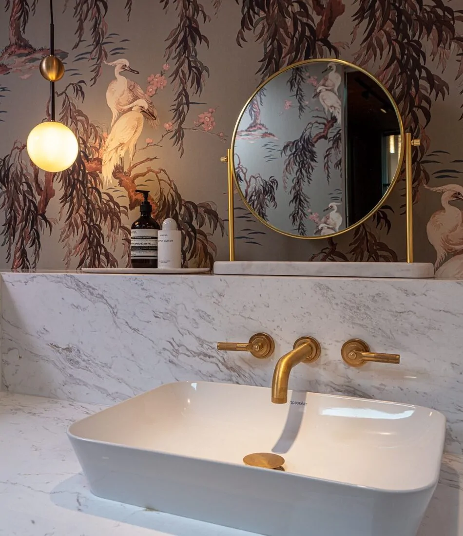 Marble sink surround with brass fixtures and round freestanding mirror