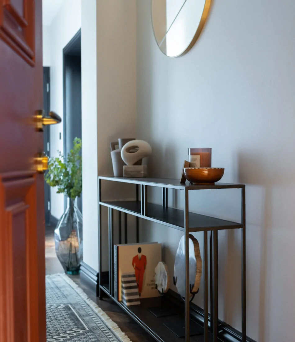 A modern console table with decorative items, including a candle, bowls, and books, stands in a well-lit entryway. A large mirror reflects the space, enhancing the visual appeal.