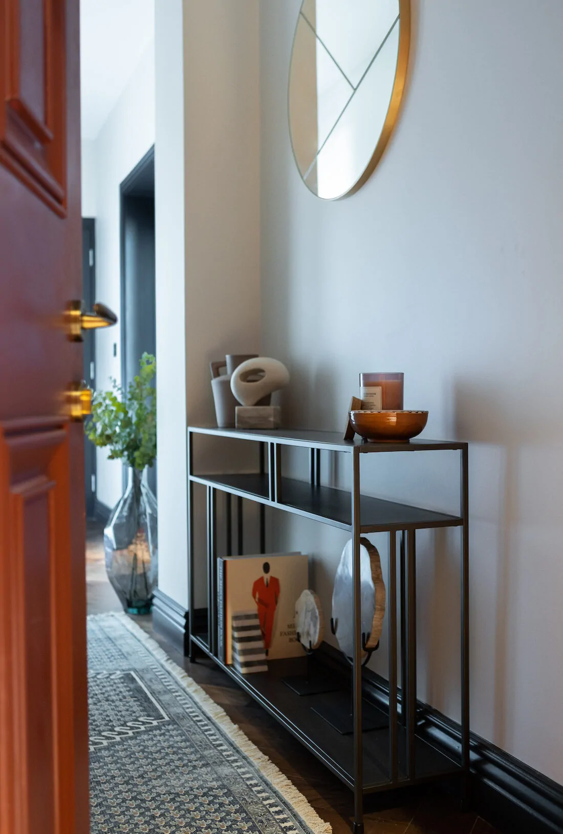 A modern console table with decorative items, including a candle, bowls, and books, stands in a well-lit entryway. A large mirror reflects the space, enhancing the visual appeal.