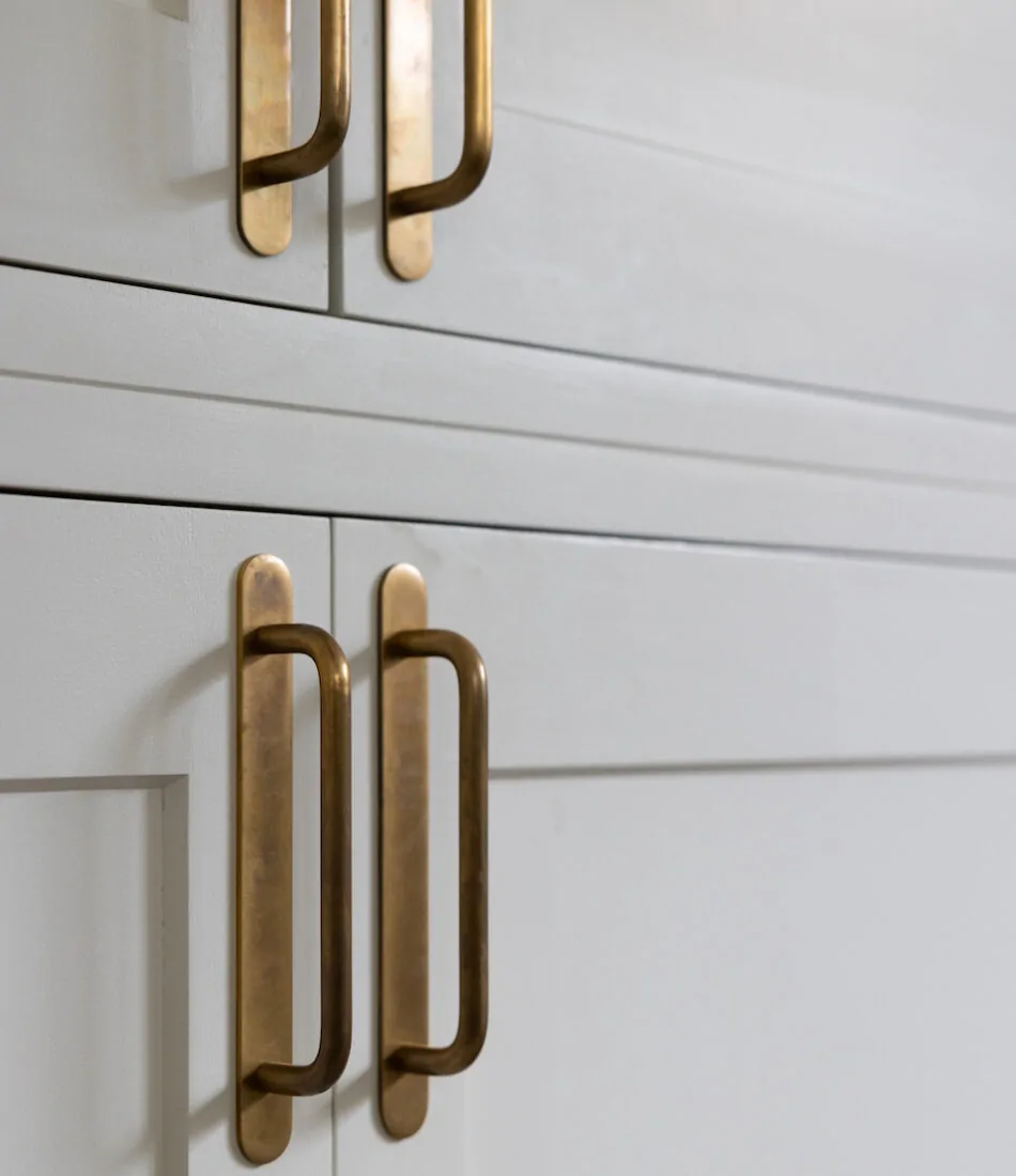 Brushed brass handles adorn a pair of cabinet doors, positioned neatly and showcasing a light gray finish. The image focuses on the elegant hardware against a minimalist backdrop.