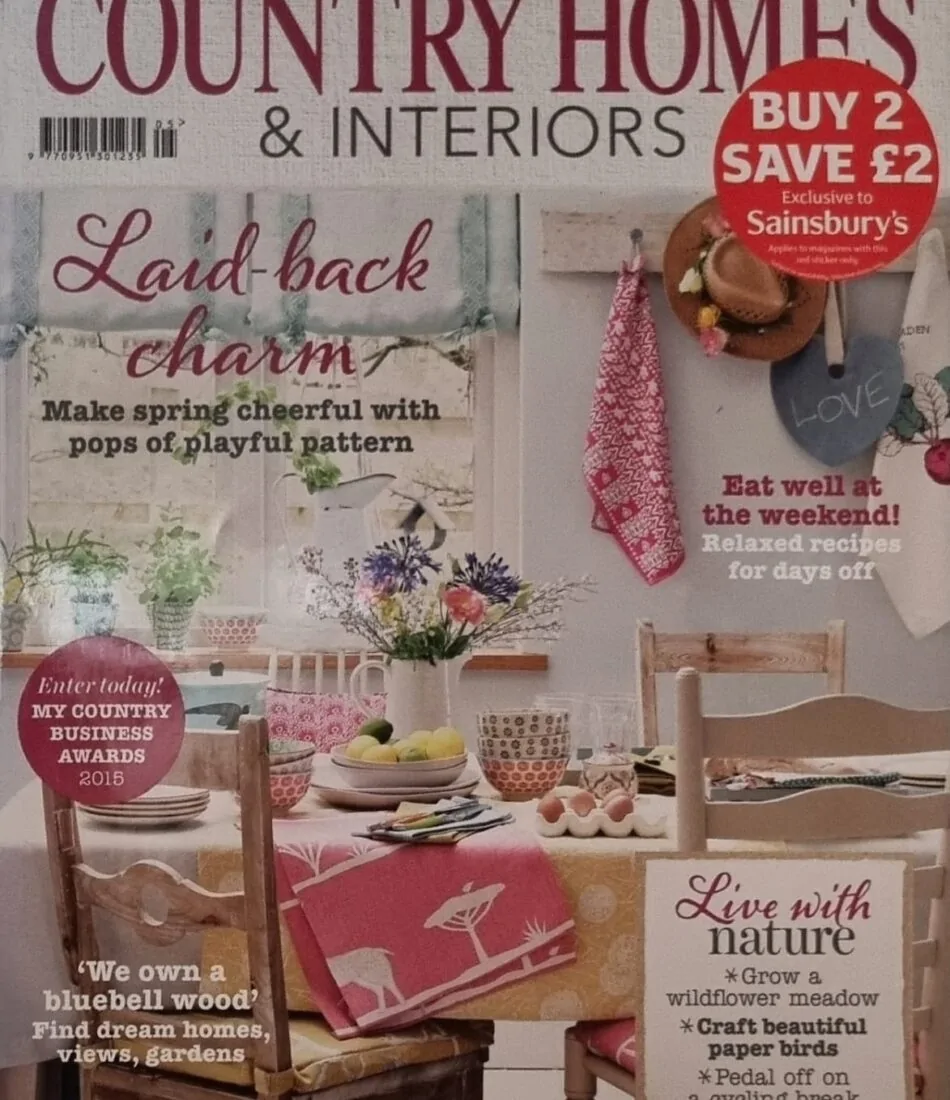 A magazine cover features a cosy dining setup with a floral tablecloth, dishes, and flowers. Text highlights themes of home decor and nature. The magazine title is "COUNTRY HOMES & INTERIORS." Additional text includes "Laid-back charm" and offers like "BUY 2 SAVE £2."