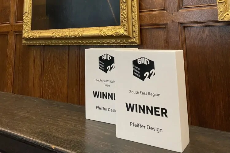 Two award plaques are displayed on a wooden shelf. One plaque states "The Anna Whitehead Prize," and the other reads "WINNER" for the "South East Region," both for "Pfeiffer Design." A framed painting is partially visible in the background.