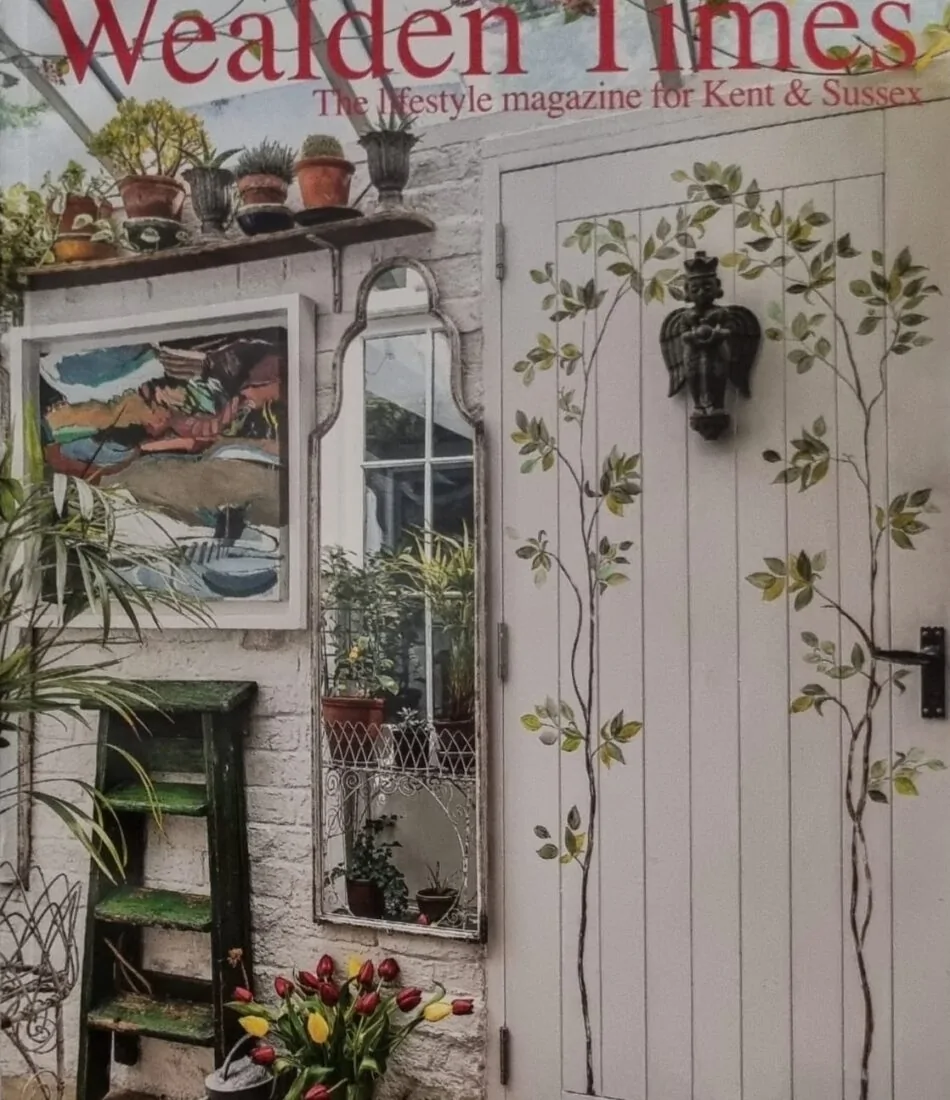 A magazine cover featuring a white door adorned with floral designs, a mirror reflecting greenery, and potted plants. The title "Wealden Times" is prominently displayed at the top.