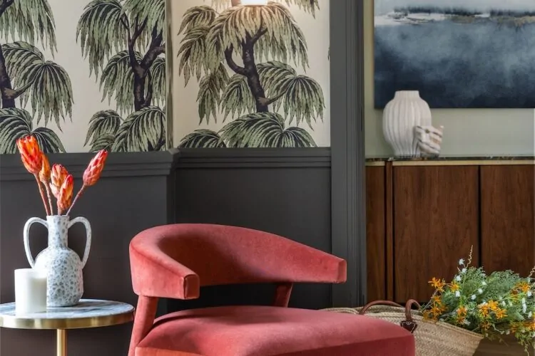 Art Deco Inspired Entrance Hall designed by Pfeiffer Design. Art deco inspired wallpaper, half height panelling and glazed French double doors in deep green. Bronze obscured glass wall lights. A soft red occasion chair with side table with dried flowers in a double handled vase.