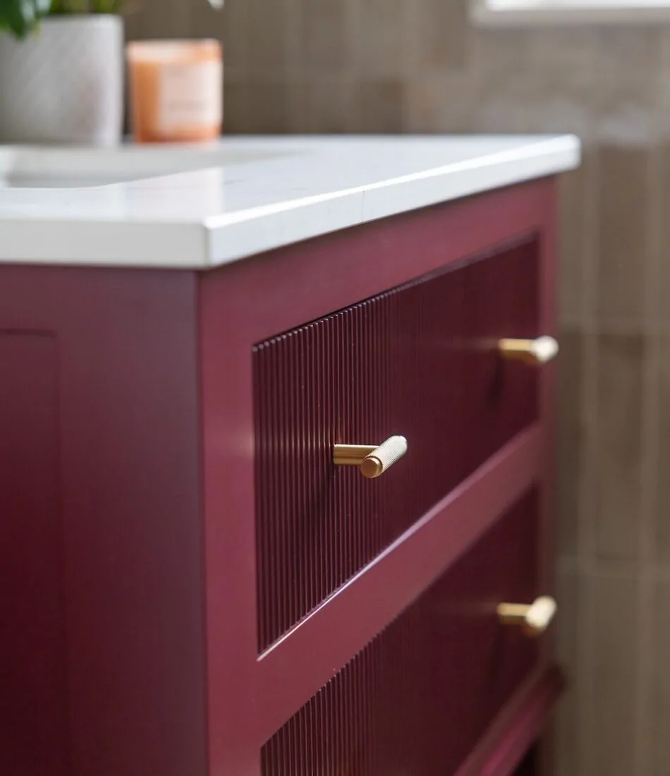 Art Deco Inspired Guest Bathroom/ Downstairs WC designed by Pfeiffer Design. Textured wallpaper in pale pink with half height tiling below, deep burgundy vanity unit with gold accent handles, warm wall lighting in a guest downstairs bathroom WC