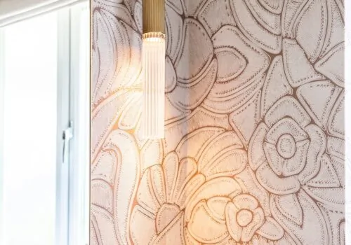 Гостевая ванная комната в стиле ар-деко с туалетом на первом этаже, дизайн от Pfeiffer Design. Текстурированные обои бледно-розового цвета с плиткой половинной высоты, тумба насыщенного бордового цвета с золотыми ручками, тёплое настенное освещение в гостевой ванной комнате с туалетом на первом этаже.