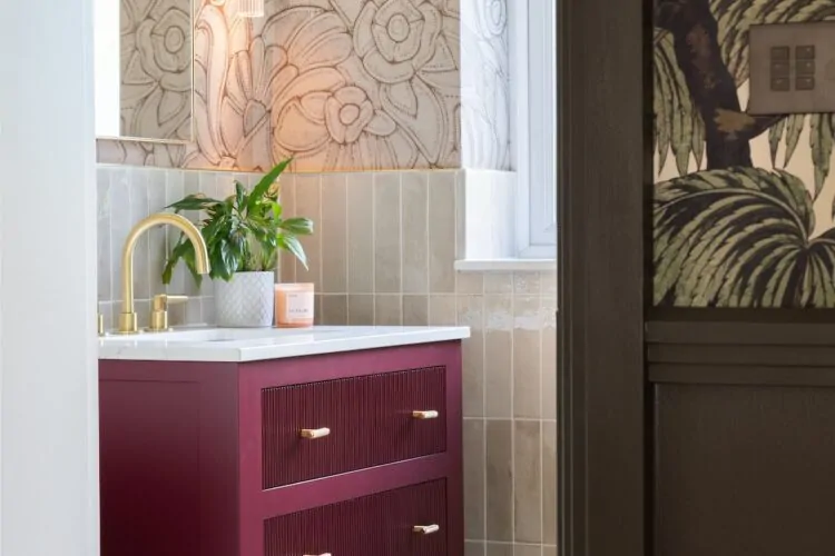 Art Deco Inspired Guest Bathroom/ Downstairs WC designed by Pfeiffer Design. Textured wallpaper in pale pink with half height tiling below, deep burgundy vanity unit with gold accent handles, warm wall lighting in a guest downstairs bathroom WC