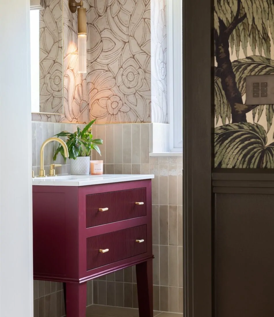 Art Deco Inspired Guest Bathroom/ Downstairs WC designed by Pfeiffer Design. Textured wallpaper in pale pink with half height tiling below, deep burgundy vanity unit with gold accent handles, warm wall lighting in a guest downstairs bathroom WC