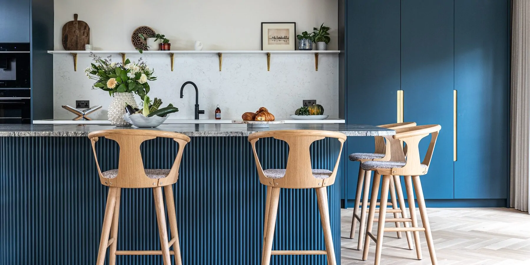 Art Deco Inspired Bespoke Kitchen made by our bespoke joiners, designed by Pfeiffer Design. Blue fluted timber island, breakfast cabinet, insert handles, light timber chevron flooring with timber bar stools