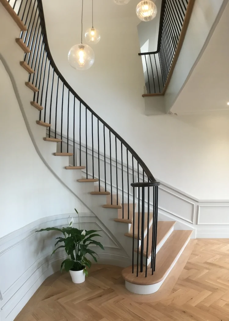 Winding staircase with black hand rail and wooden steps.