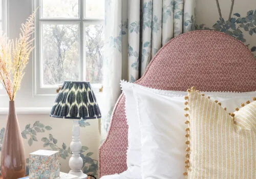 Upholstered headboard in red fabric with pattern drenched curtain and walls behind in matching wallpaper and curtain fabric